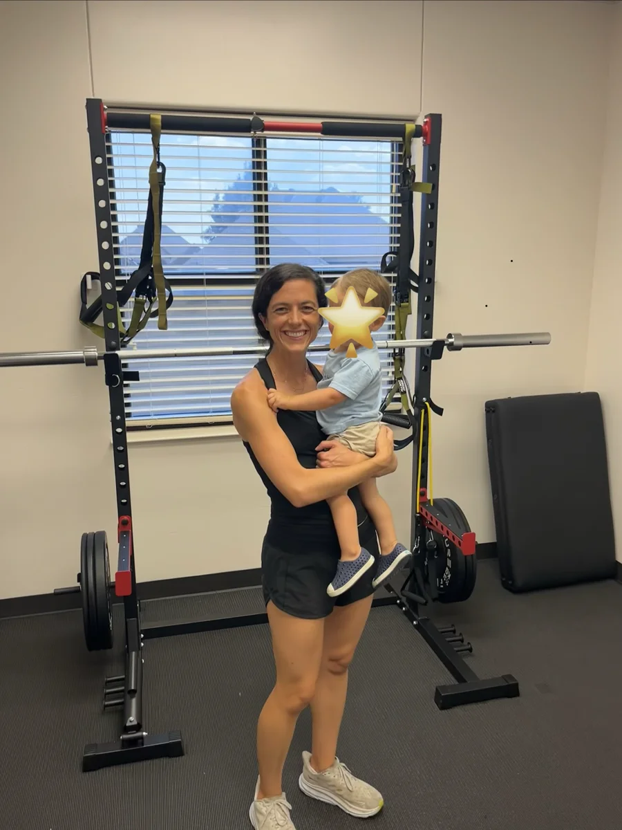 Caroline holding a child beside strength-training equipment in the studio.